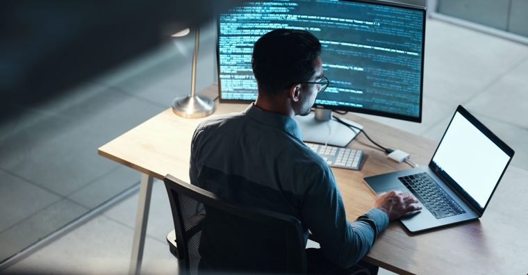 Un homme assis à son bureau avec deux écrans d'ordinateurs devant lui