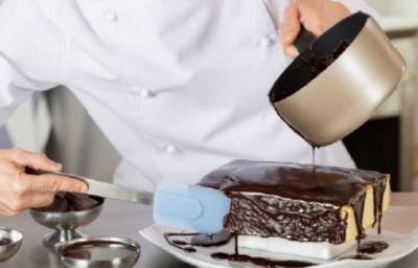 Un apprenti pâtissier versant du chocolat fondu sur un gâteau