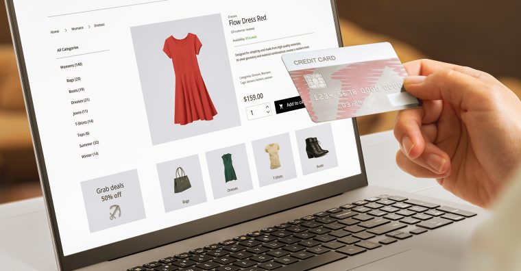 Personne faisant un achat avec une carte de crédit sur une page web de commerce électronique présentant des vêtements pour femme sur l’écran d’un ordinateur portable.